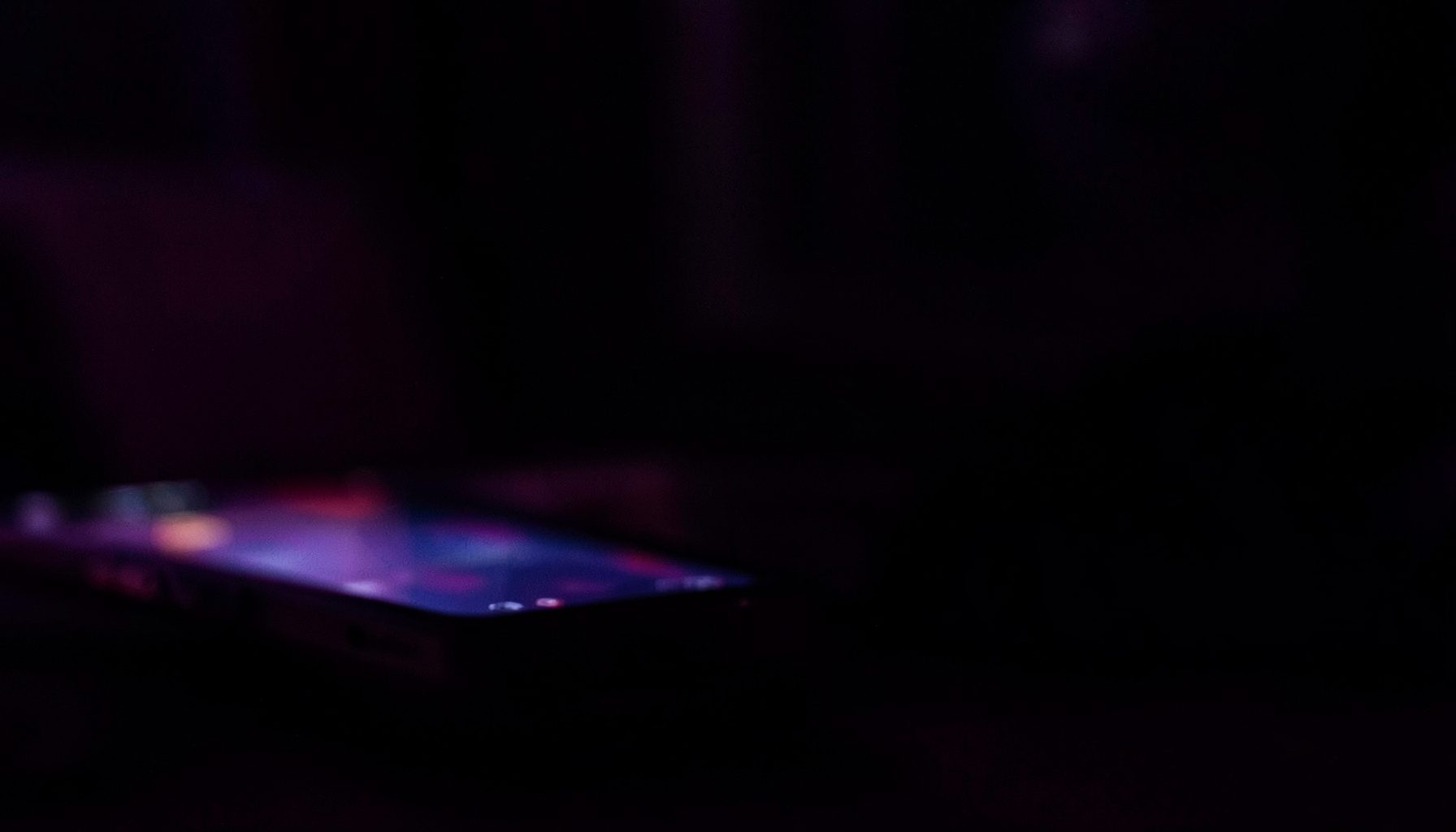 Dark atmospheric background with deep purple and black tones, a subtle glow suggesting a mobile phone screen in a dimly lit room, moody and intimate