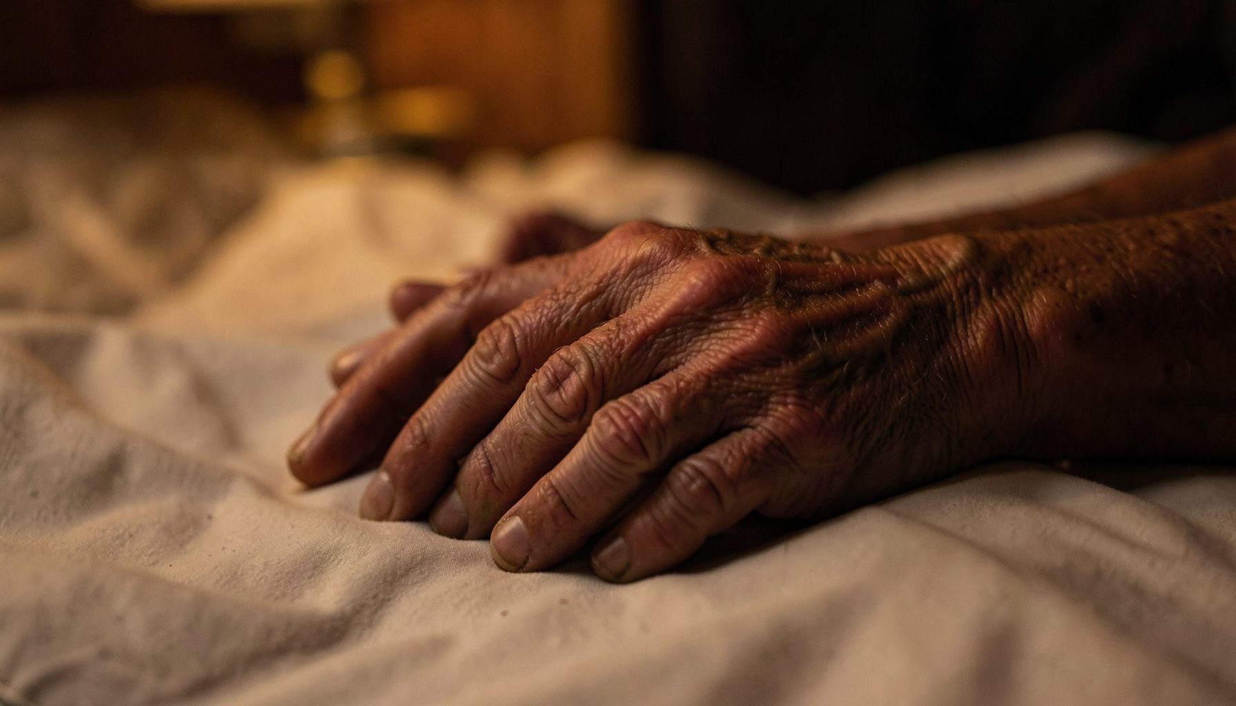 Contrast of aged hands and smooth skin, dim bedroom with amber glow